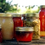 Homemade preserves sitting on a rustic table outside. Pickes, tomatoes, appplesauce, etc.