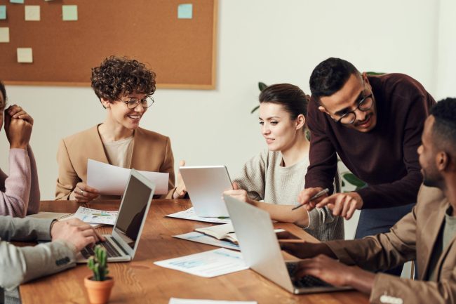 Group of people collaborating around a conference table with laptops and documents during a team meeting.