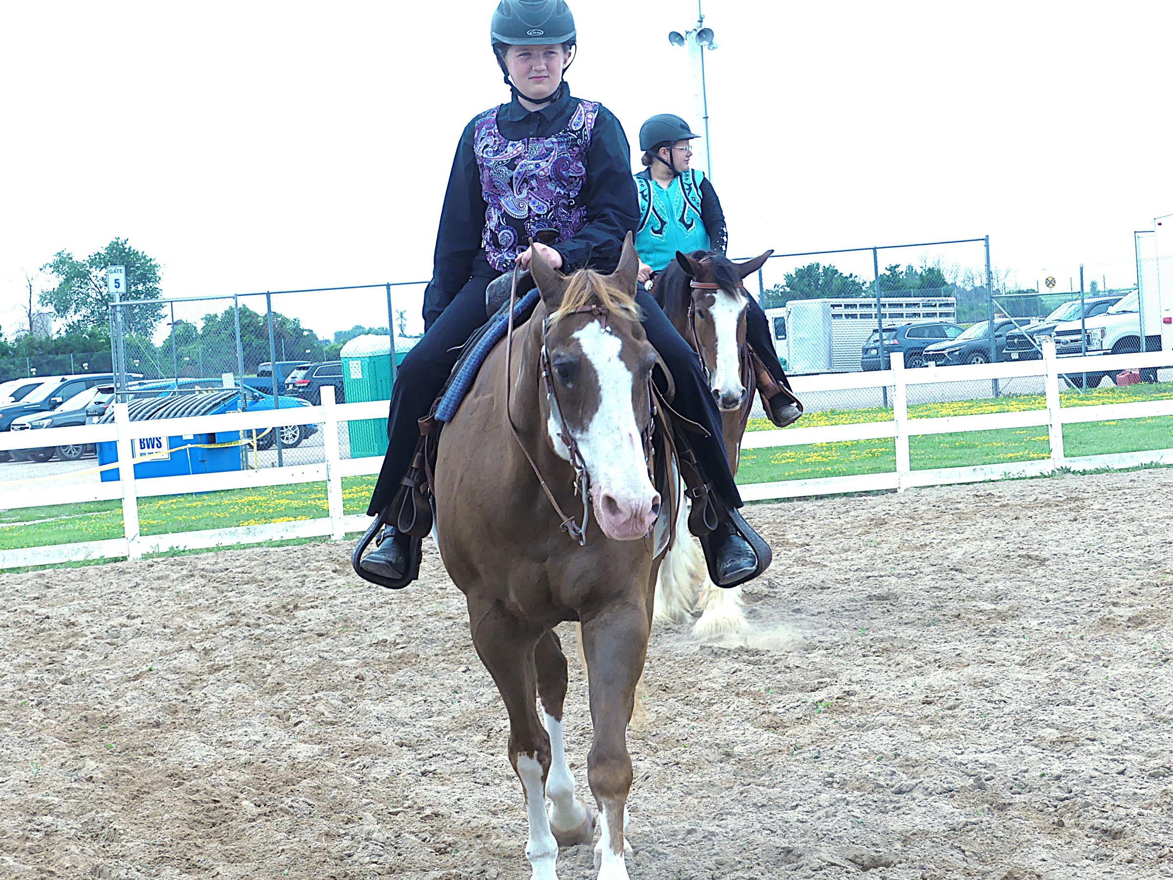 Youth riders on horseback participate in a riding activity in an outdoor arena.